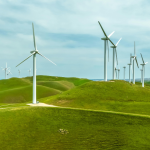 Wind turbines stand on rolling green hills under a blue, cloudy sky in a wind farm setting.
