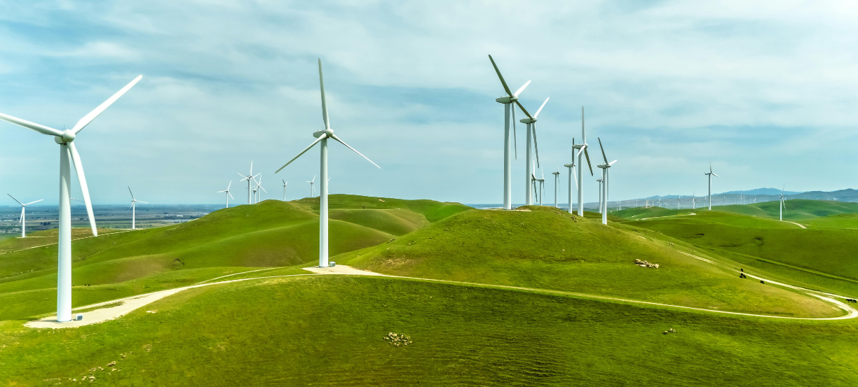 Wind turbines stand on rolling green hills under a blue, cloudy sky in a wind farm setting.